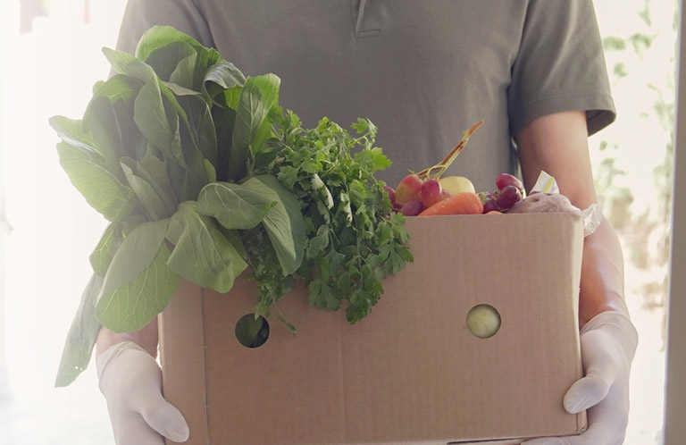 Person holding box of fresh vegetables
